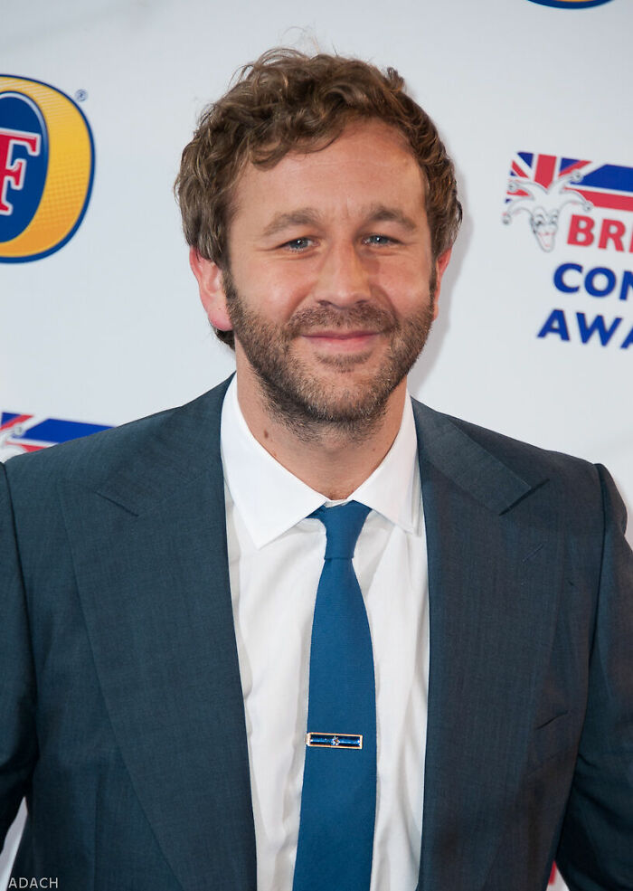A portrait of actor Chris O'Dowd wearing a suit and tie at an event, highlighting his career