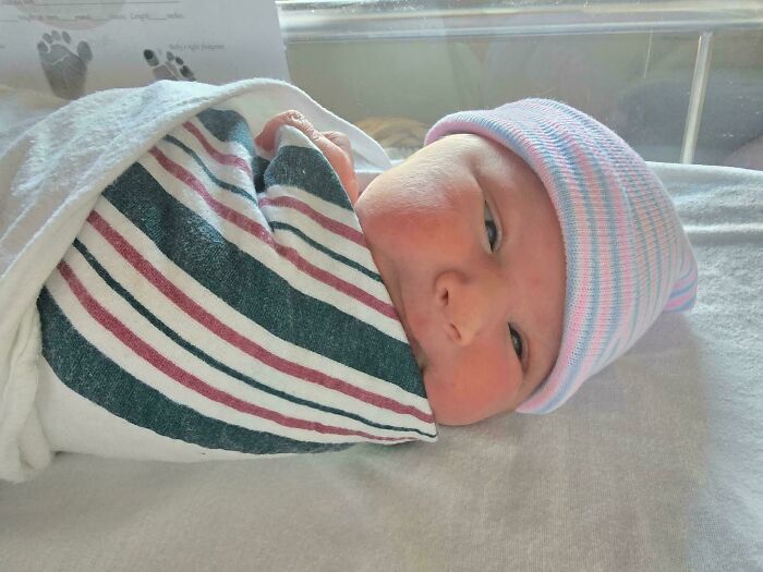 A cozy swaddled newborn baby wearing a striped hat, capturing wholesome dads fatherhood moments.