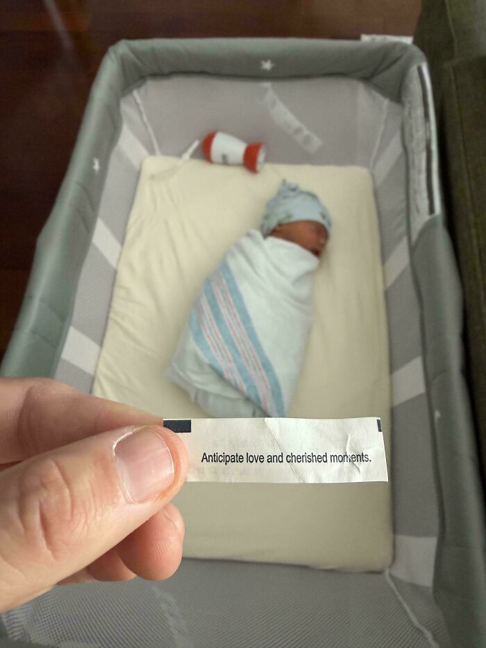 A sleeping newborn baby in a bassinet next to a fortune cookie paper, representing wholesome dads moments.
