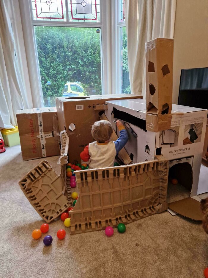 A toddler playing inside a large custom cardboard fort, showcasing creative wholesome dads.