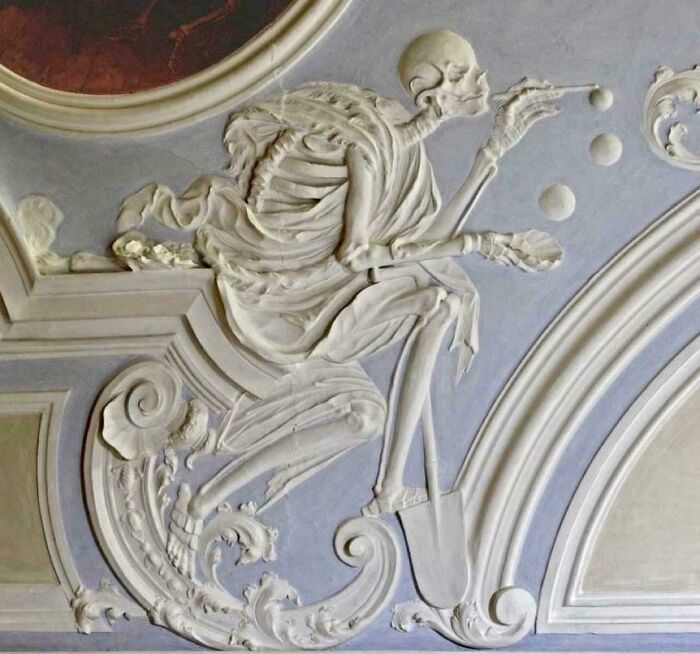 Sculpted skeleton figure playing with balls on historical ceiling art