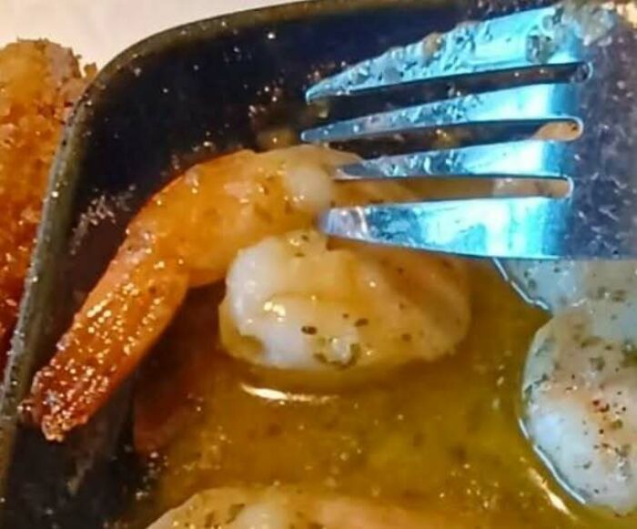 Shrimp in butter looking like a face staring with a fork.