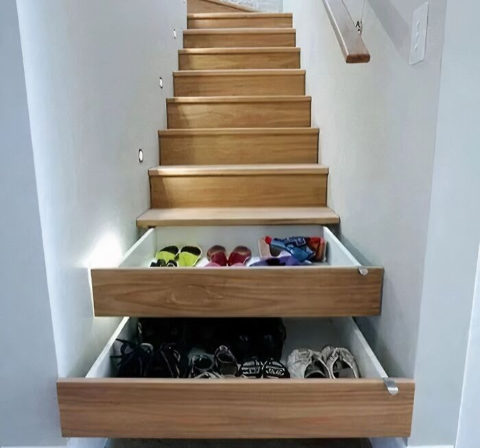 Under-stairs storage drawers pulled out to show shoes, demonstrating clever wooden creations for space-saving.