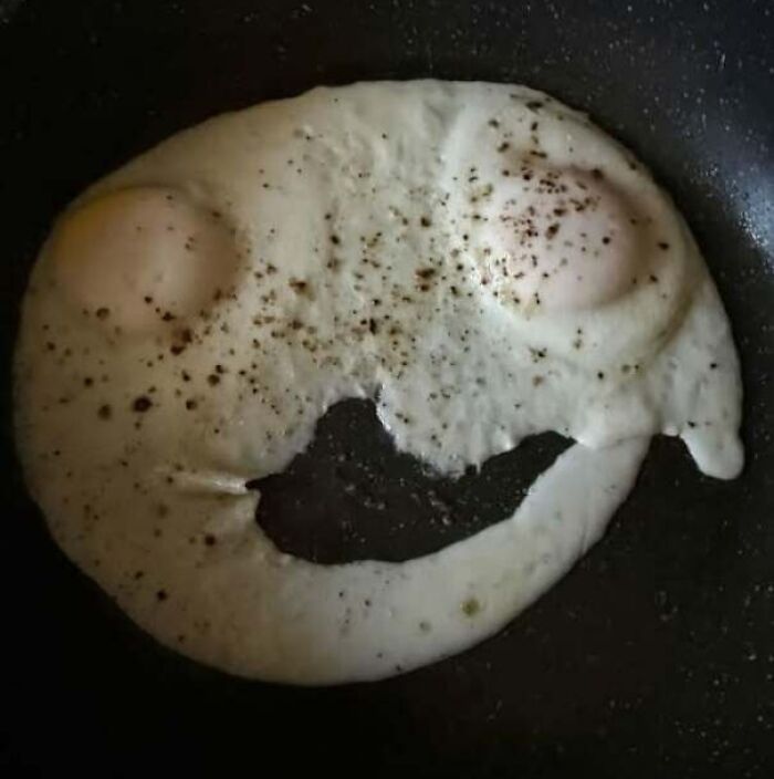 Two fried eggs on pan with pepper creating a face with eyes and mouth