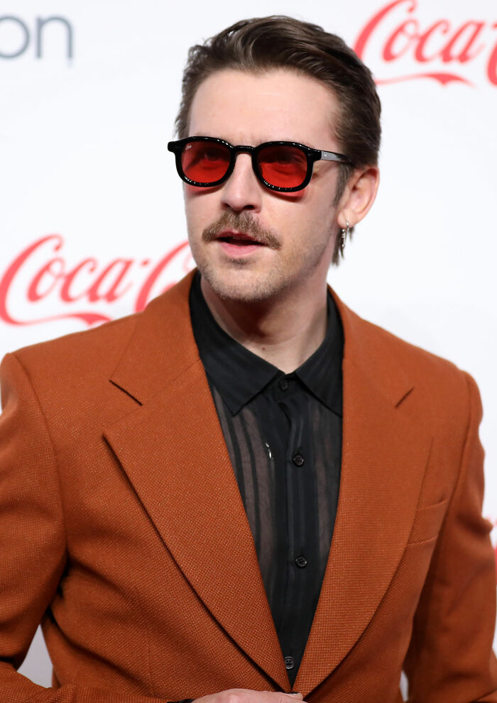 Actor Dan Stevens wearing red sunglasses and a rust-orange blazer at a red carpet event