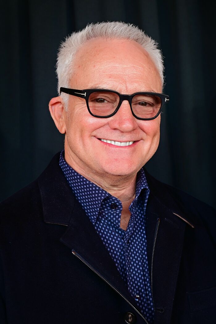Smiling portrait of actor Bradley Whitford wearing black glasses and a dark jacket.