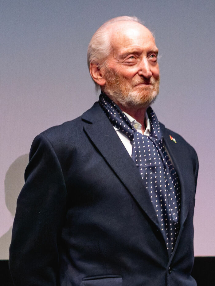 Actor Charles Dance wearing a navy suit jacket and polka dot cravat scarf