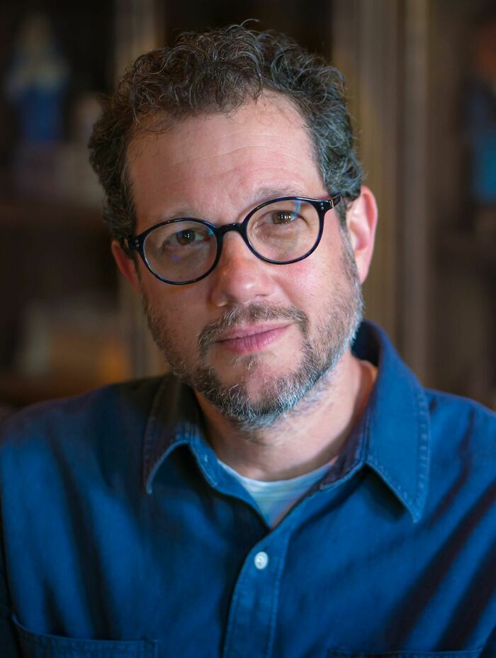 Close-up portrait of composer Michael Giacchino wearing glasses and a blue button-up shirt.