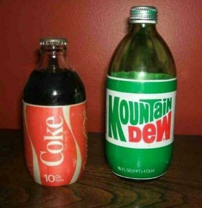 Old glass bottles of vintage Coke and Mountain Dew sodas on wooden surface