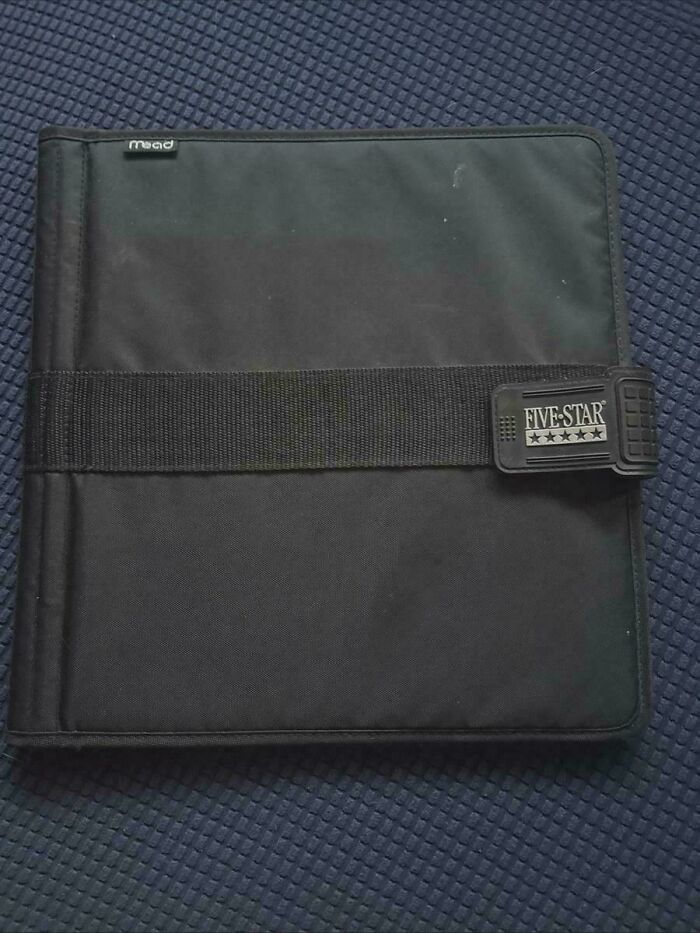 Black Five Star brand binder with a strap on a textured blue surface