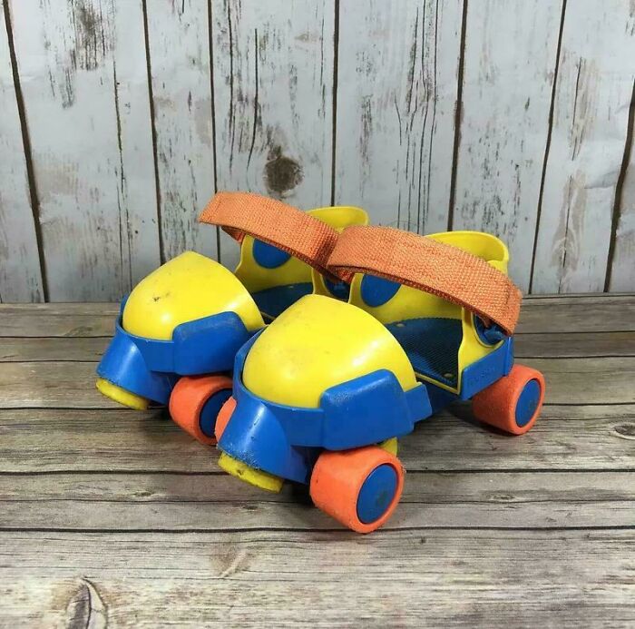 Vintage kids roller skates in yellow, blue, and orange colors on wooden floor