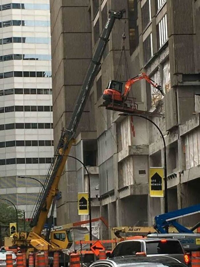 Construction fail with excavator dangerously suspended by crane on building facade