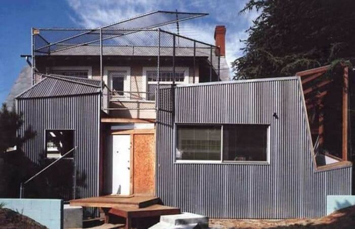 A house featuring mismatched corrugated metal siding and chain link fencing, showcasing construction fails