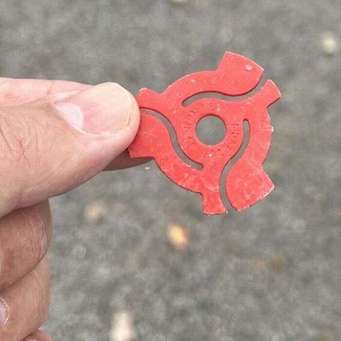 Hand holding a red plastic 45 rpm adapter for vinyl records