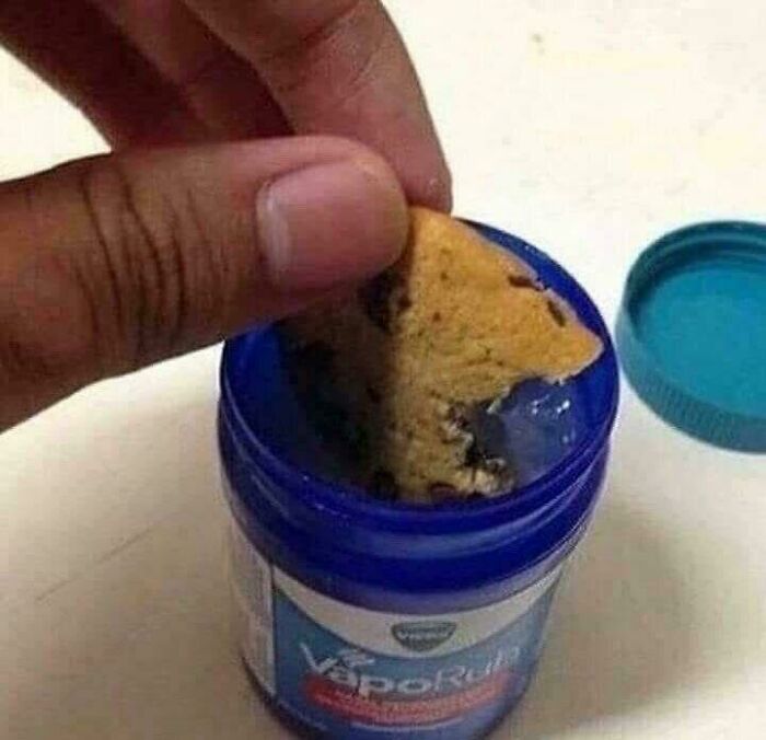 A hand dipping a chocolate chip cookie into a container of Vicks VapoRub, one of many cursed images.