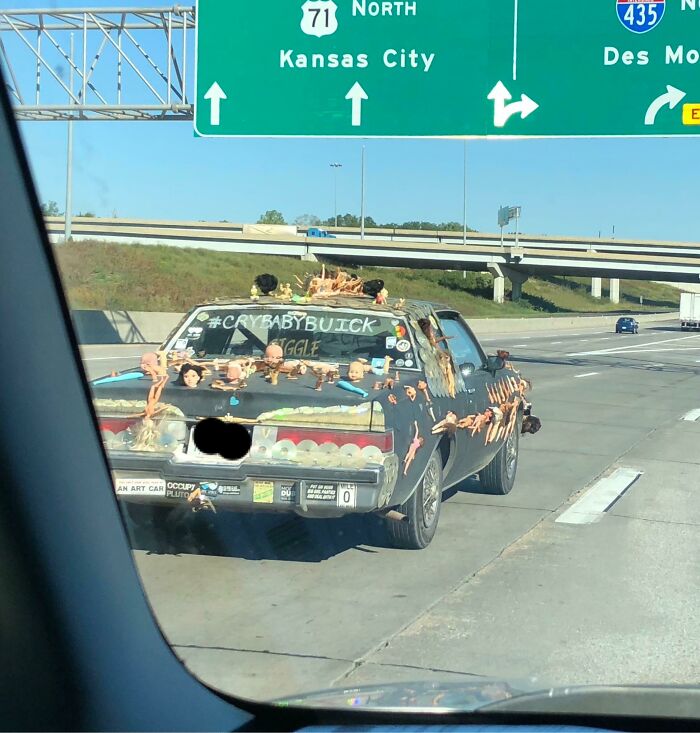 Car covered in plastic dolls and strange objects driving on highway, an example of cursed images.