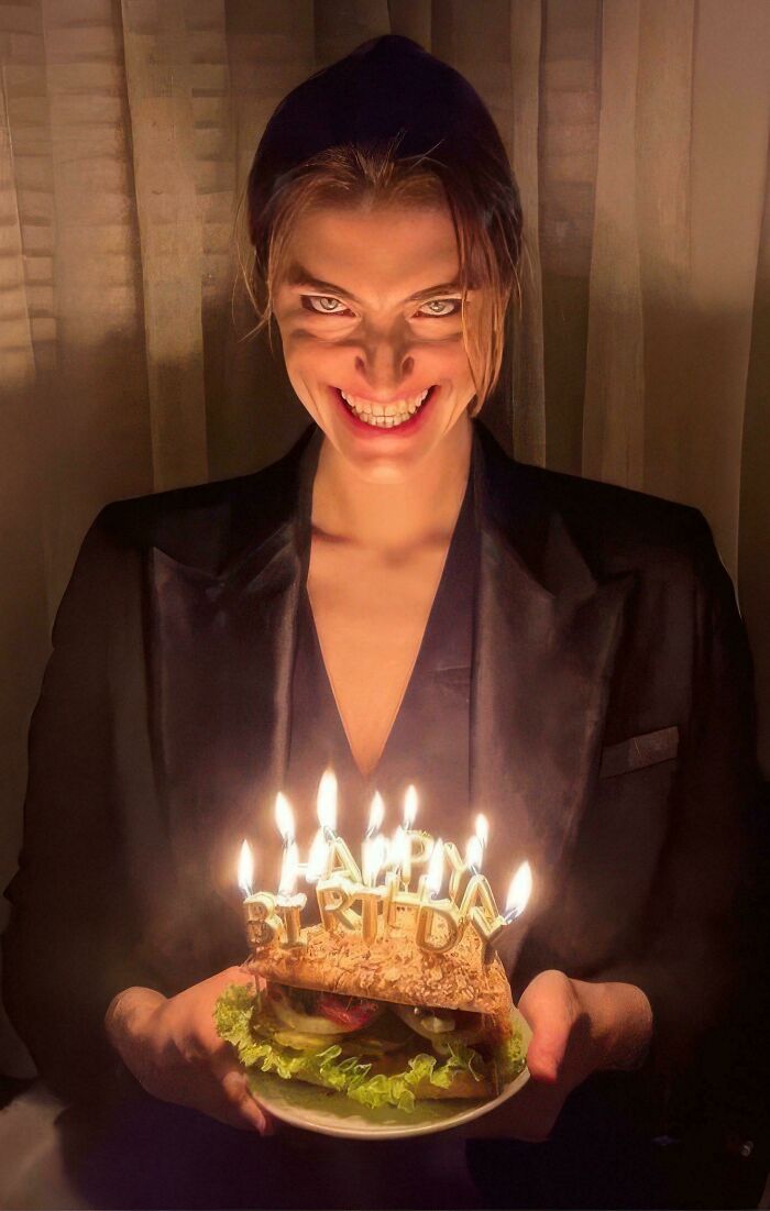 Woman with a creepy smile holding a birthday sandwich with lit candles, featured in cursed images.