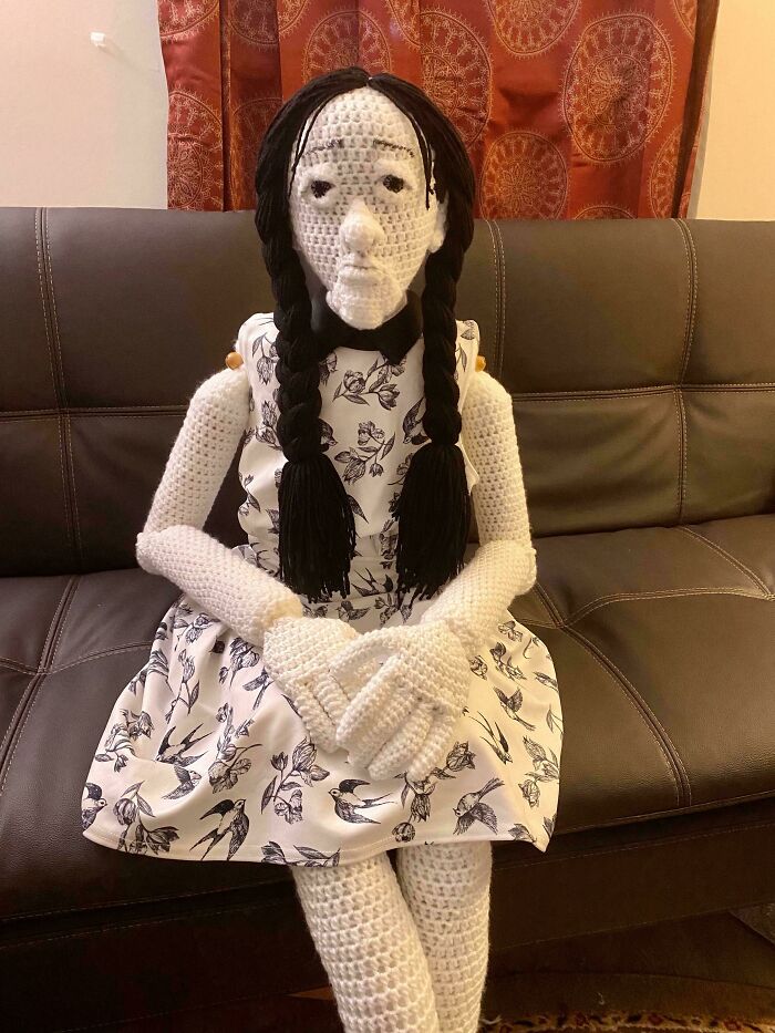 A creepy life-sized knitted doll sitting on a brown leather couch, listed in cursed images.
