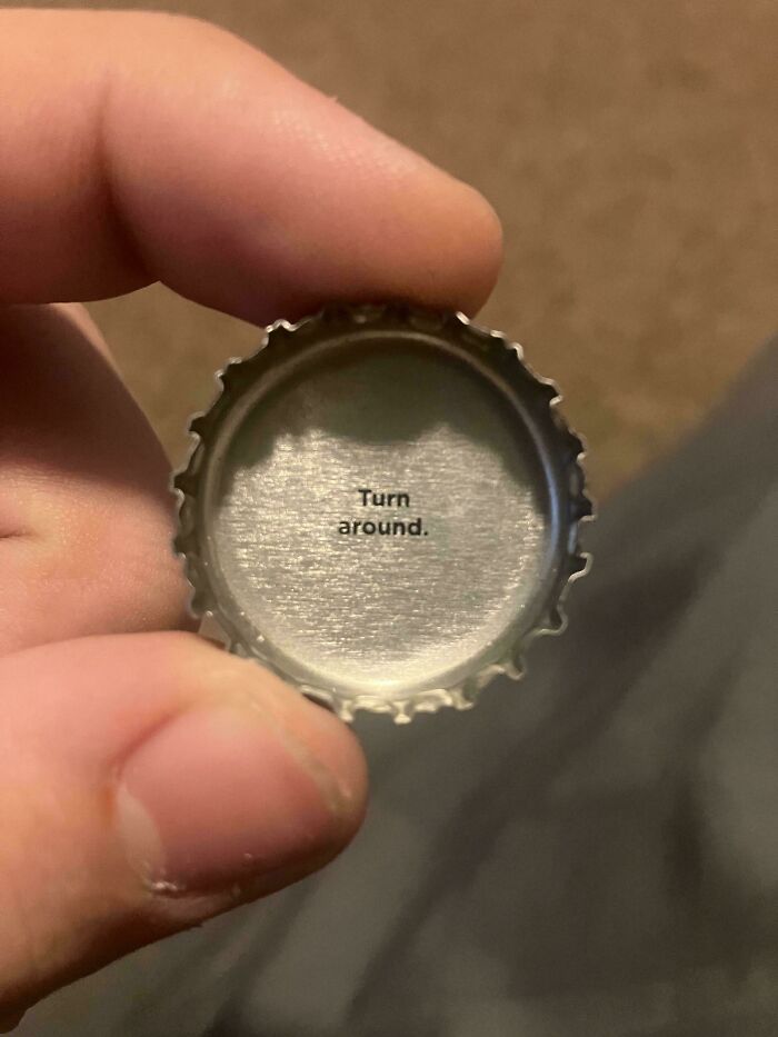 A bottle cap held in a hand reading Turn around inside, serving as one of many cursed images.