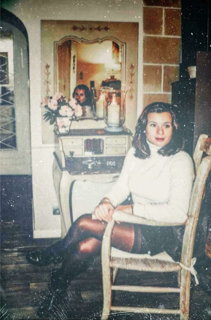 A woman sitting in a chair with an eerie figure reflecting in the mirror behind her, among creepy photos.