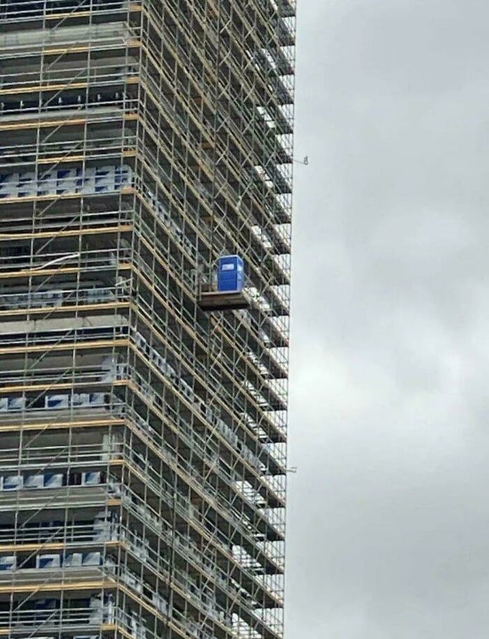 A porta potty suspended high up on a construction scaffolding platform in cursed images.