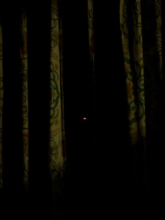 Glowing red eyes visible in the dark behind curtains, adding to eerie creepy photos