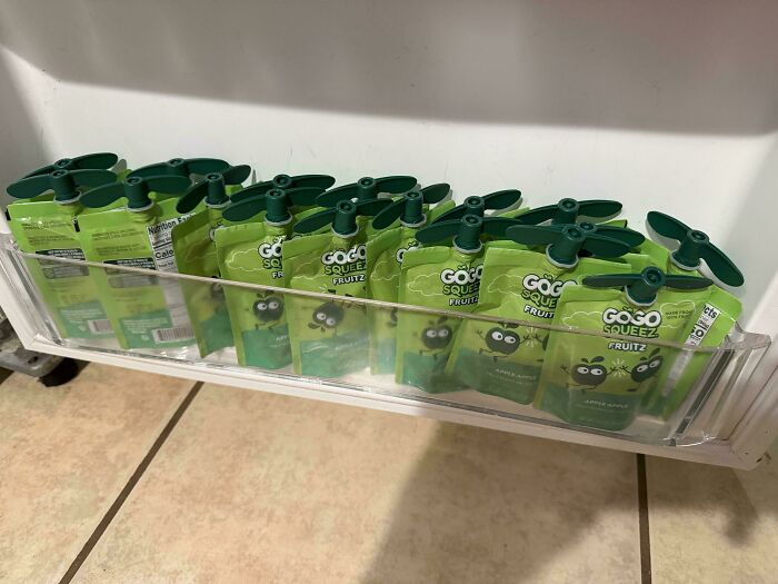 A refrigerator shelf neatly stocked with green applesauce pouches prepared by a dad for his kids snacks.
