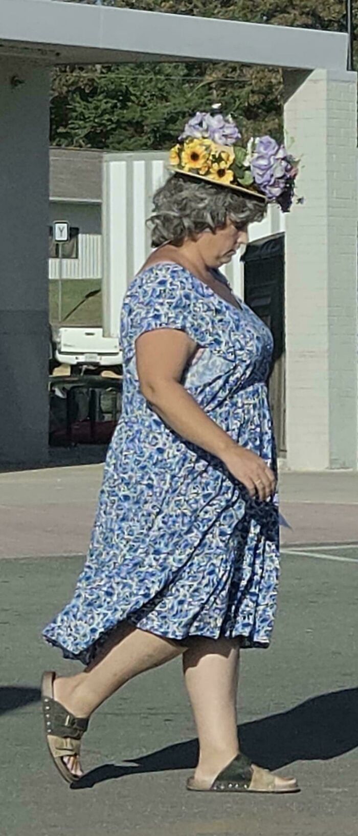 Woman wearing floral hat and blue dress walking outside Walmart