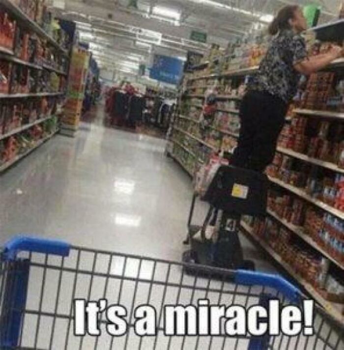 Person standing on motorized cart reaching high shelf in Walmart aisle with shopping cart in foreground