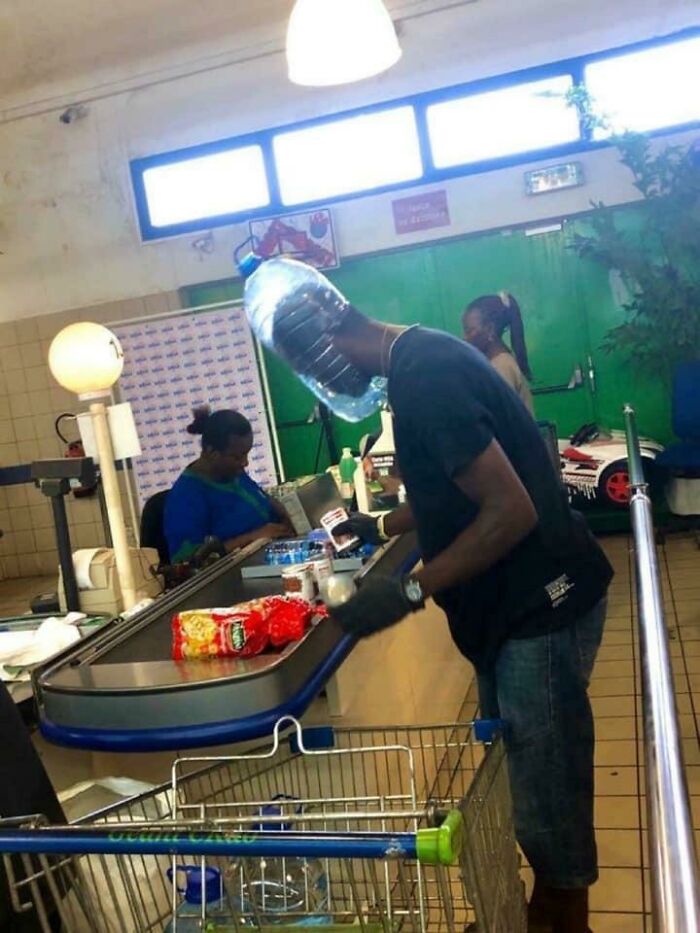 Man shopping at Walmart checkout with plastic water jug on head and groceries in cart