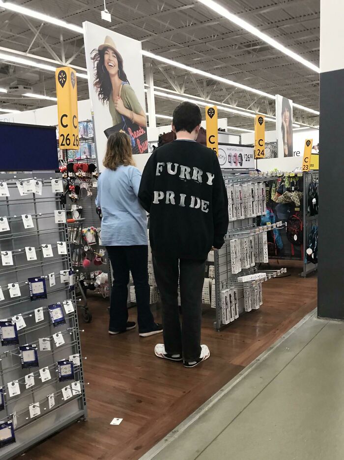 Two shoppers inside Walmart store aisle, one wearing furry pride sweatshirt