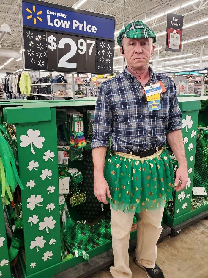 Walmart employee wearing green plaid hat and festive green skirt under low price sign