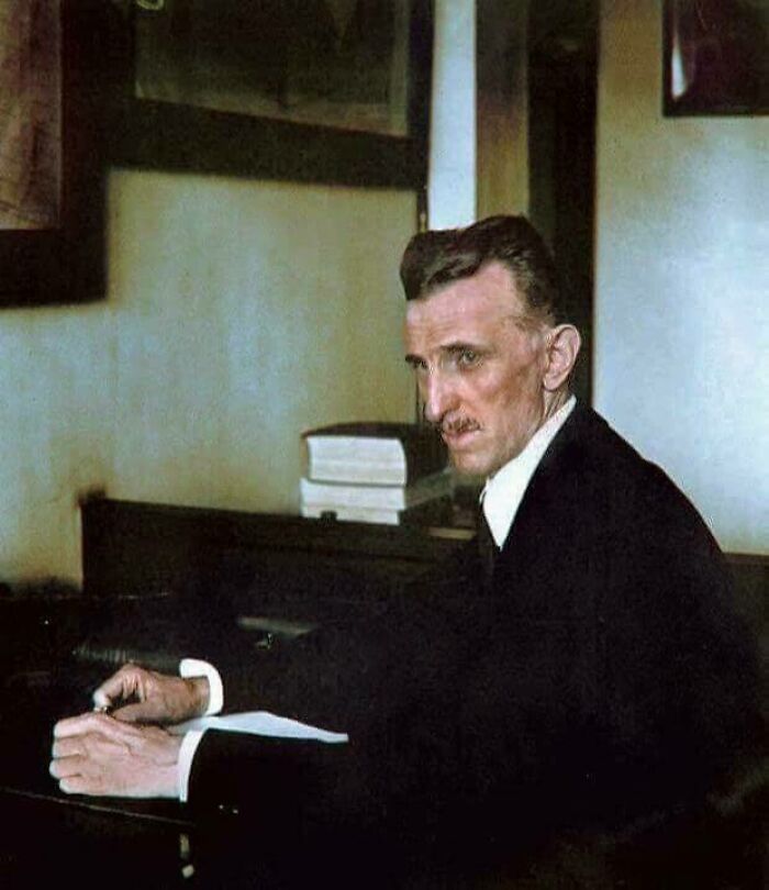 Colorized rare historical photo of Nikola Tesla sitting at a desk