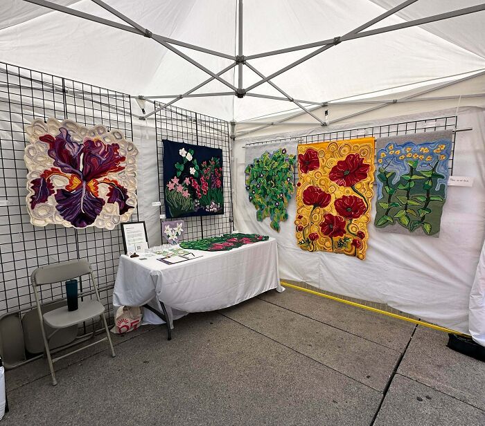 Art exhibit of colorful crochet floral wall hangings in white tent