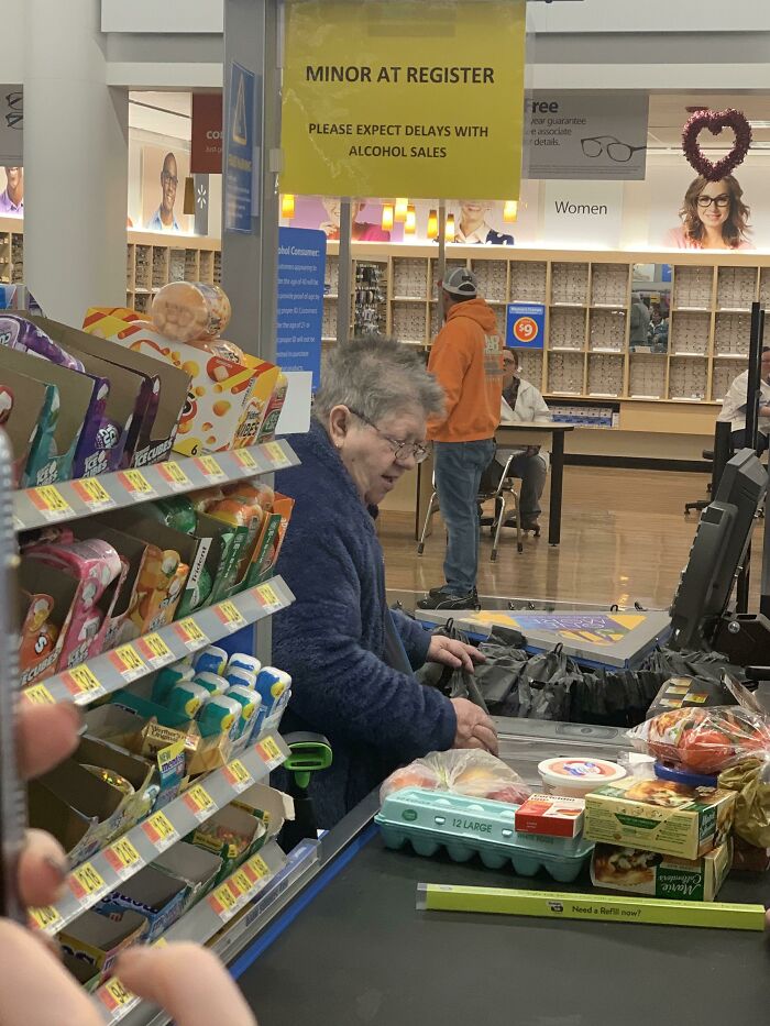 Elderly woman checking out groceries at Walmart register with snacks nearby