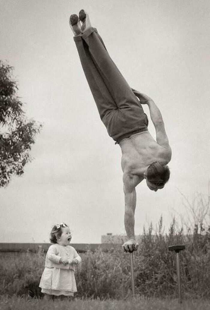 Vintage historical photo of a man performing handstand to impress a child