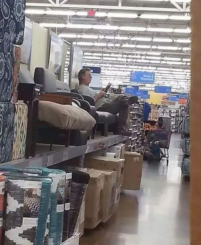 Man sitting and reading in Walmart furniture aisle with rugs and boxes nearby