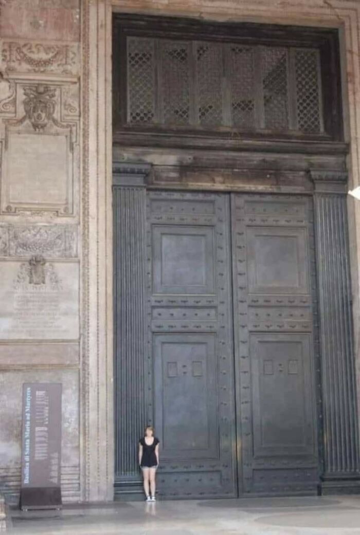 Rare historical photo showing a woman standing beside an enormous ancient door for scale