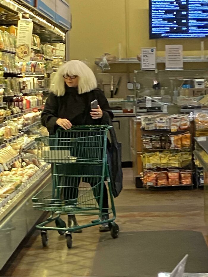 Woman with white wig and glasses shopping with cart in Walmart grocery aisle