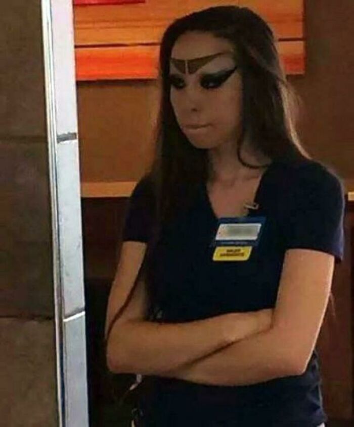 Walmart employee with heavy black eyebrow and eye makeup standing with arms crossed