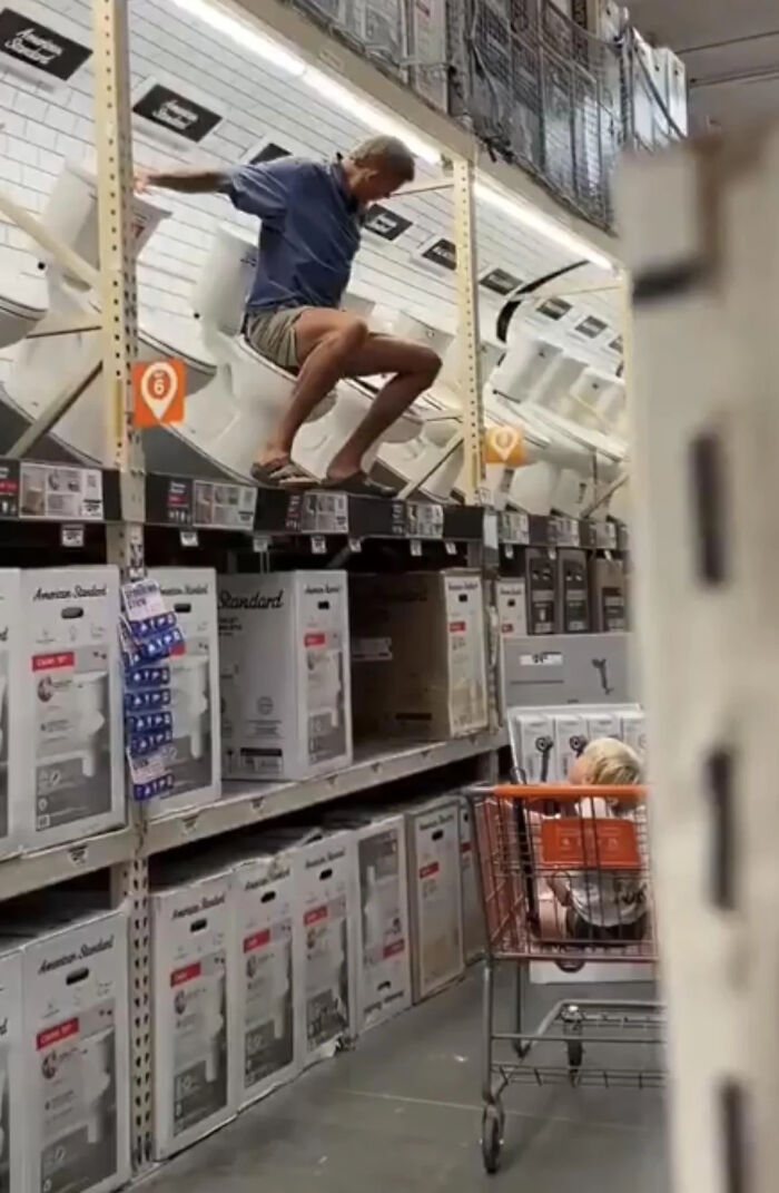 Man sitting on display toilets while child watches from shopping cart at Walmart