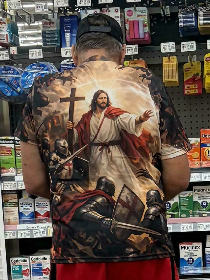 Person wearing a Walmart shirt with Jesus and knights artwork standing by pharmacy aisle