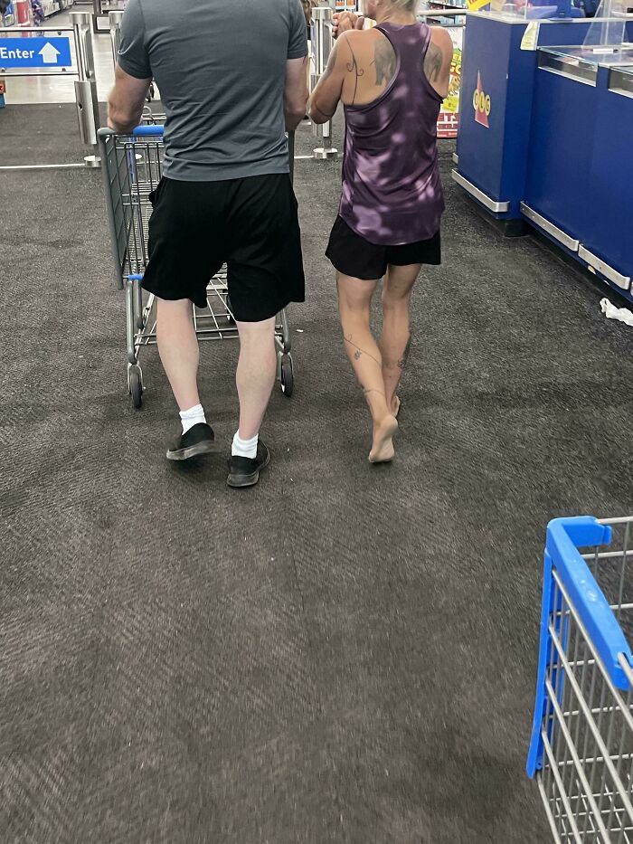 Couple walking down Walmart aisle with shopping cart from rear view