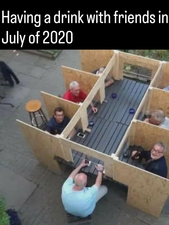 Friends sitting in wooden social distancing booths at an outdoor table, from photos and facts about history.