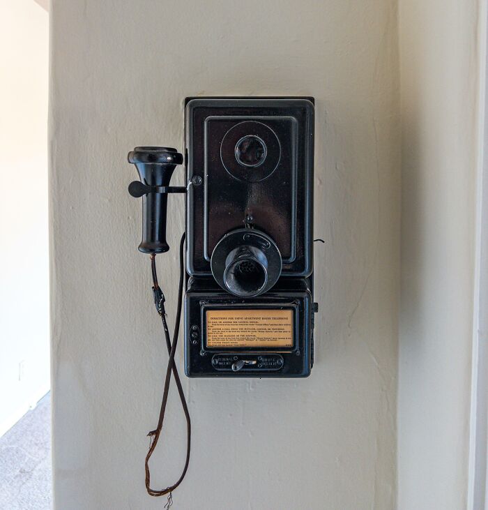 Black antique wall-mounted telephone with handset on beige wall
