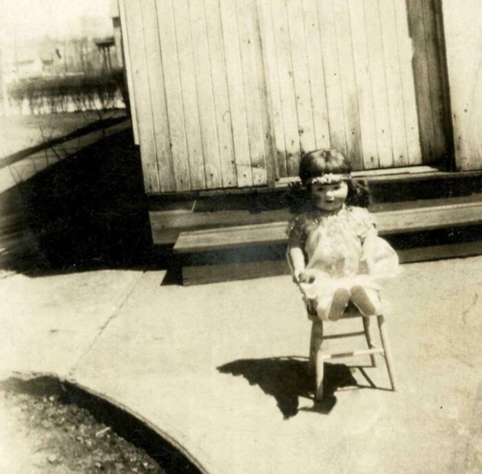 Old rare historical photo of a doll sitting on a chair outside a building