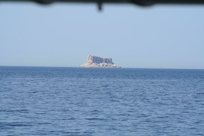 Distant rocky island in calm deep-water sea under clear sky