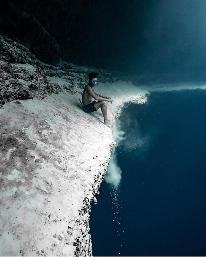 Person sitting underwater beside a deep-water abyss cliff