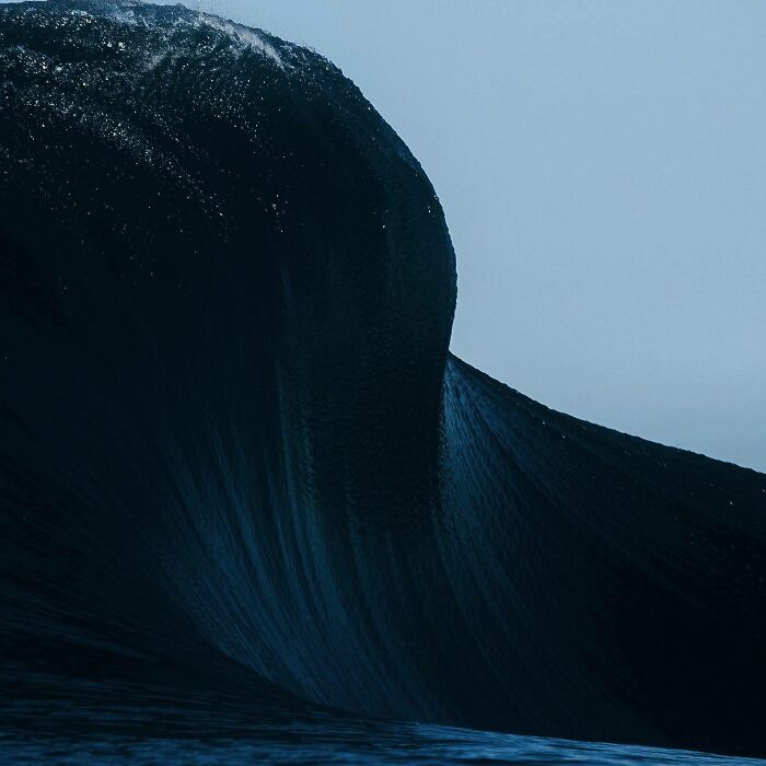 Close-up of a dark curling deep-water wave under a pale sky