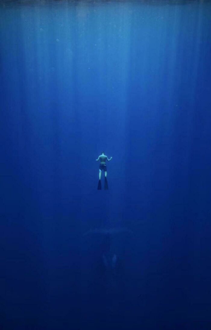 Diver descending into deep blue water with faint shapes below